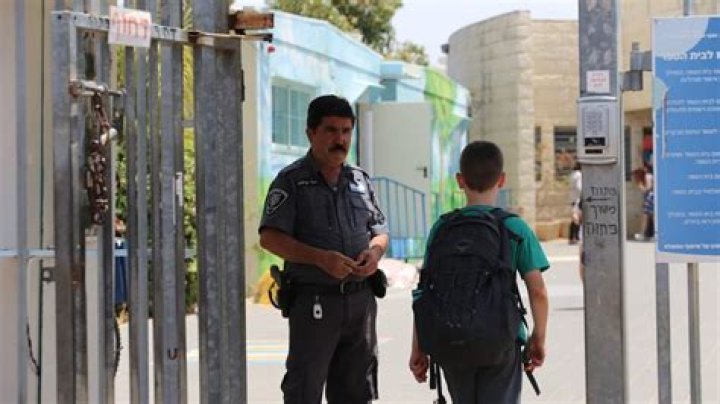 An Israeli school security officer watches on as students enter school