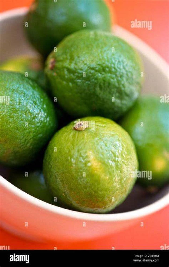 Fresh limes on a red and white gingham cloth being hand juiced in a vintage green glass juicer. | Photo: Getty Images