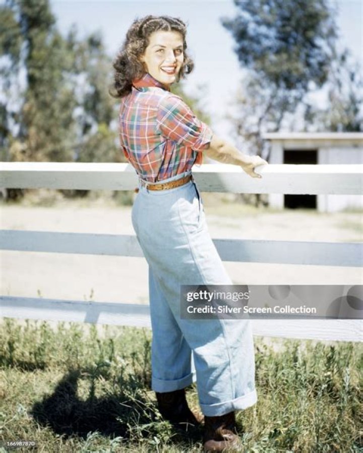 Photo of Jane Russell wearing an off-the-shoulder blue and gold dress, with a red theatre curtain behind her, circa 1955 | Photo: Getty Images