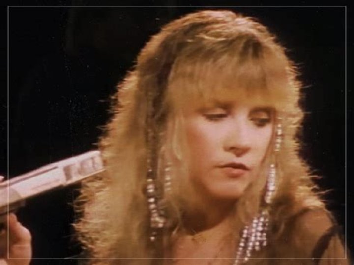 Stevie Nicks holds her hands up near her face and sings into a microphone.