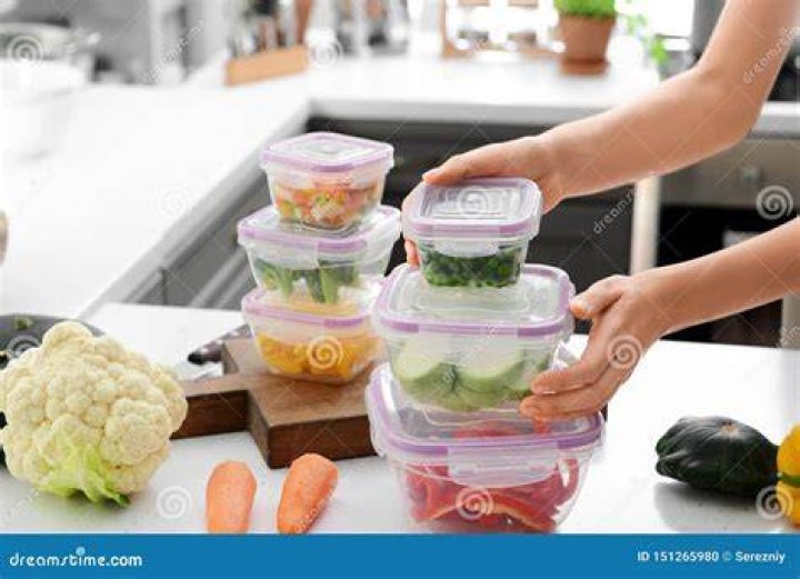 Woman holding stack of plastic containers with fresh vegetables for freezing at table in kitchen | Source: Shutterstock